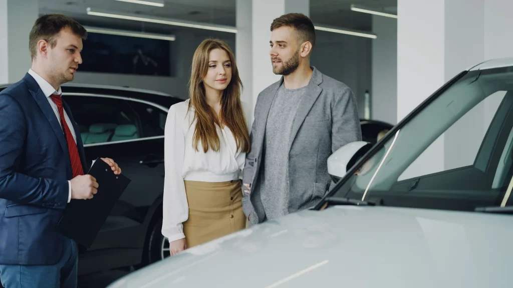 Couple talking with a salesman beside a car in a dealership