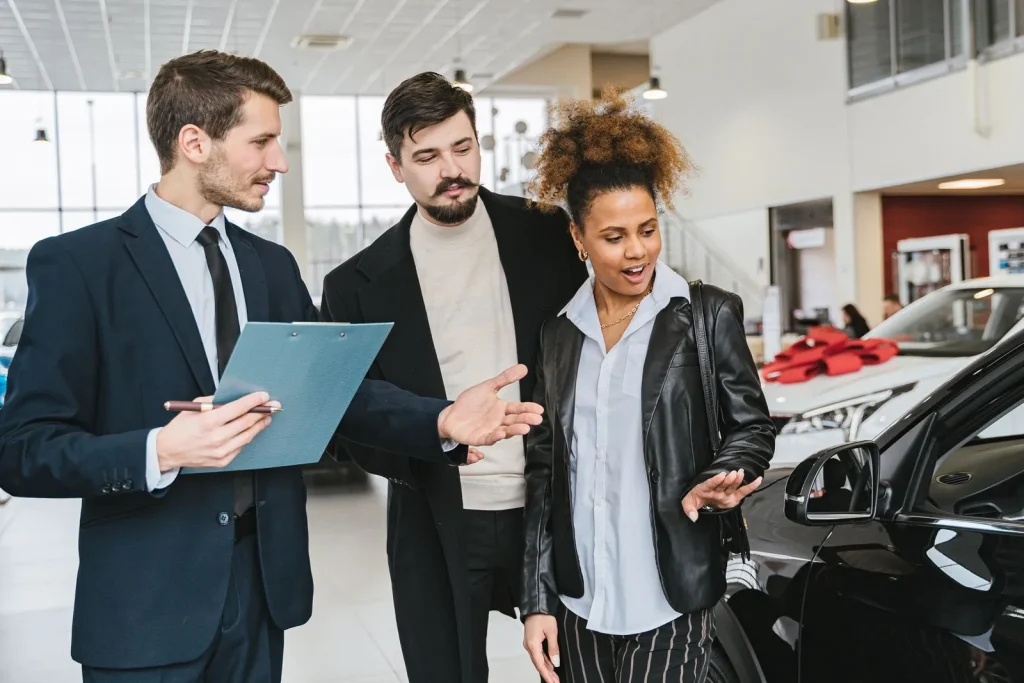 Dealership staff member with a clipboard talking to customers in a showroom