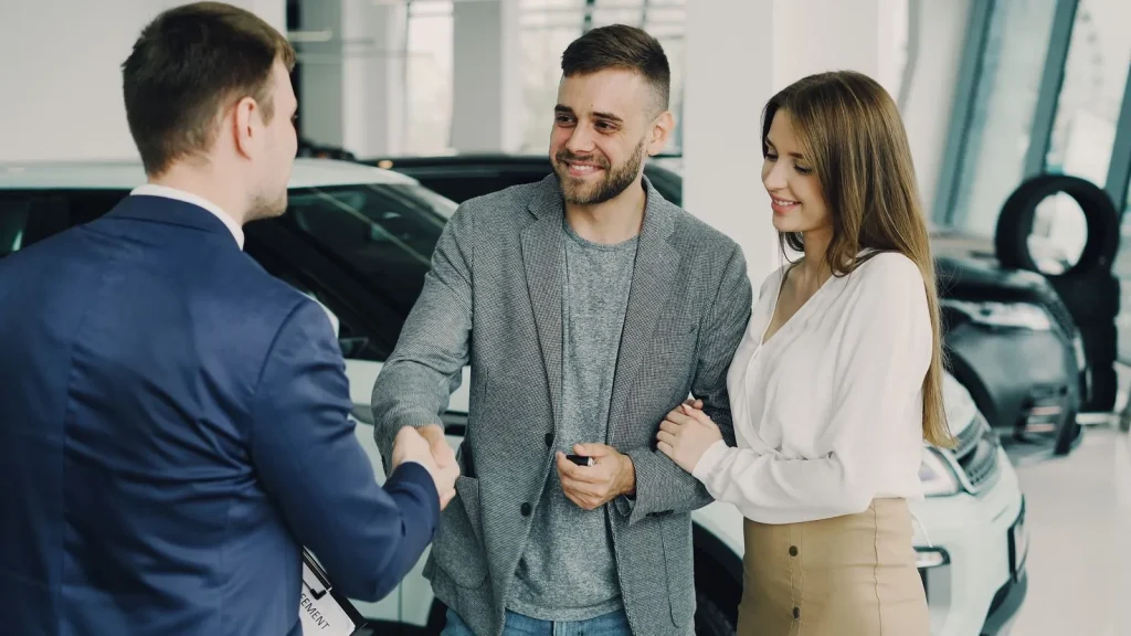 Happy couple shaking hands with a salesman after buying a car