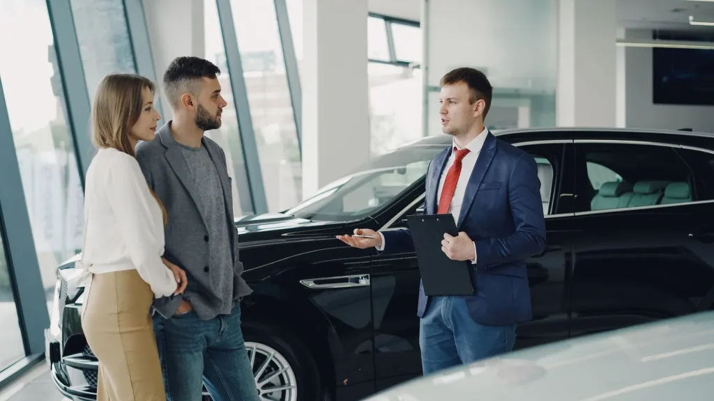 Salesman with a clipboard talking to a couple beside a car in a showroom