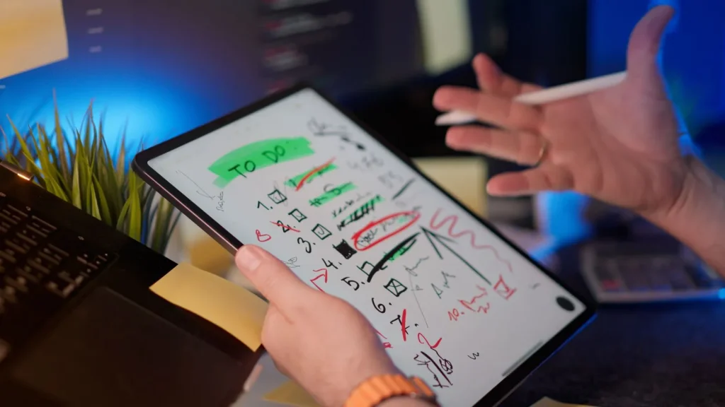 Tablet with handwritten checklist notes beside a laptop