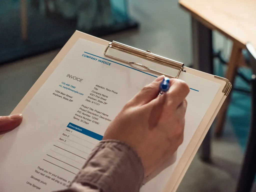 Hand holding an invoice on a clipboard with a pen
