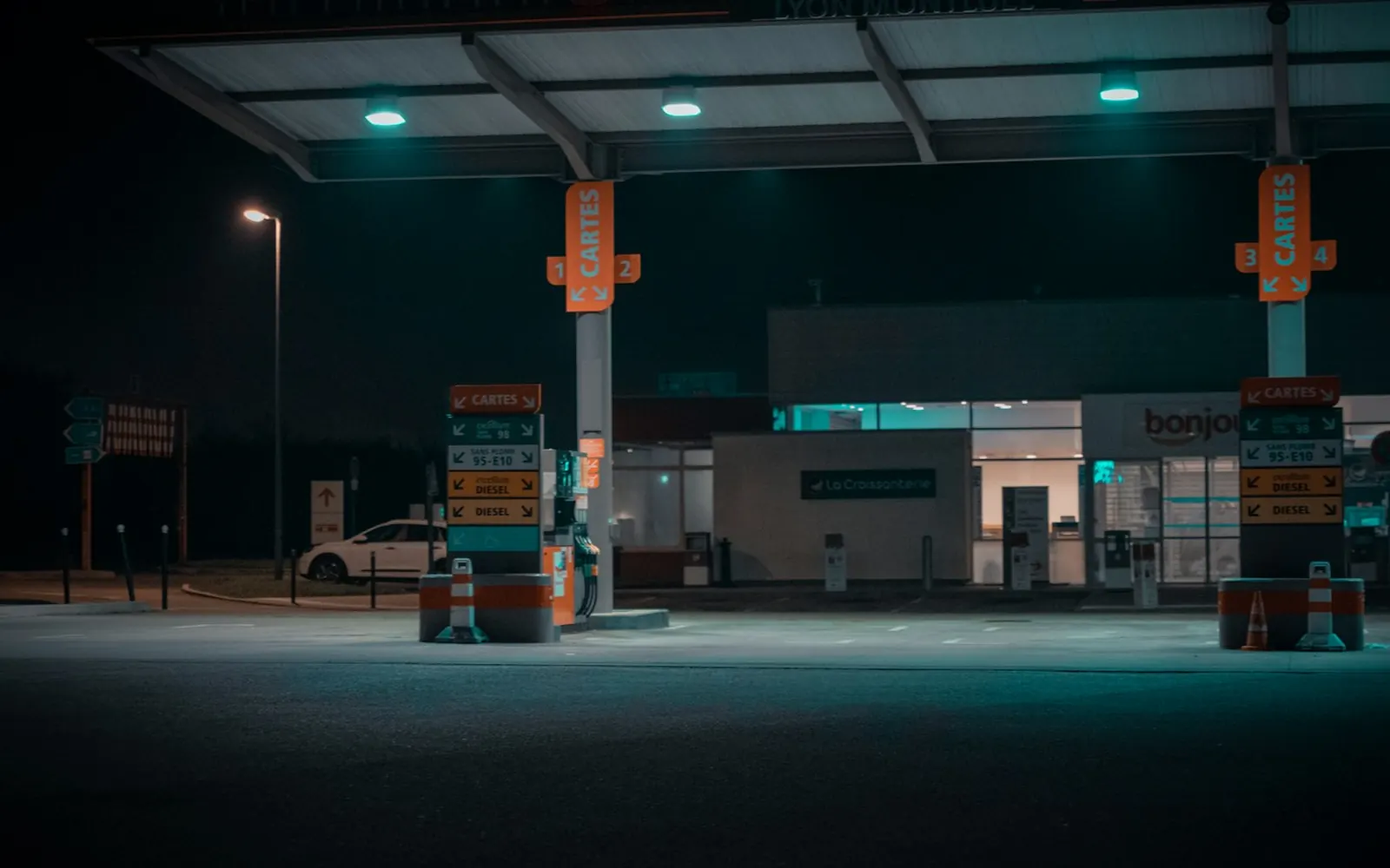 A fuel station forecourt at night, with the shop lit behind the pumps