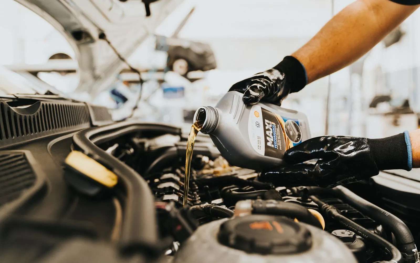 A technician in gloves pouring engine oil into a car during a service